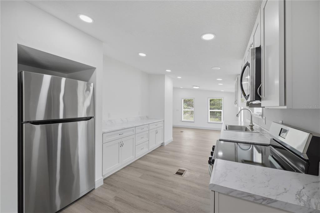 A modern kitchen features white cabinets, marble-look countertops, stainless steel appliances, and light wood flooring — 7904 CADILLAC AVENUE, HUDSON, FL
