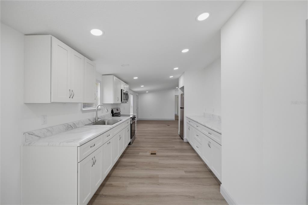 A galley kitchen features white cabinets, marble-look countertops, and light wood-style flooring — 7904 CADILLAC AVENUE, HUDSON, FL