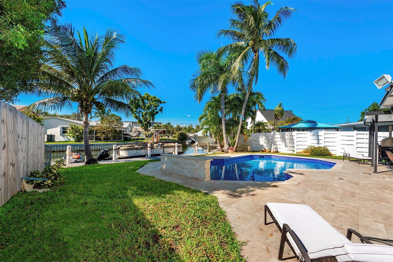 A backyard features a swimming pool, a patio, palm trees, and a boat docked on a canal — 825 Argonaut Isle, Dania Beach FL 33004, DANIA BEACH, FL