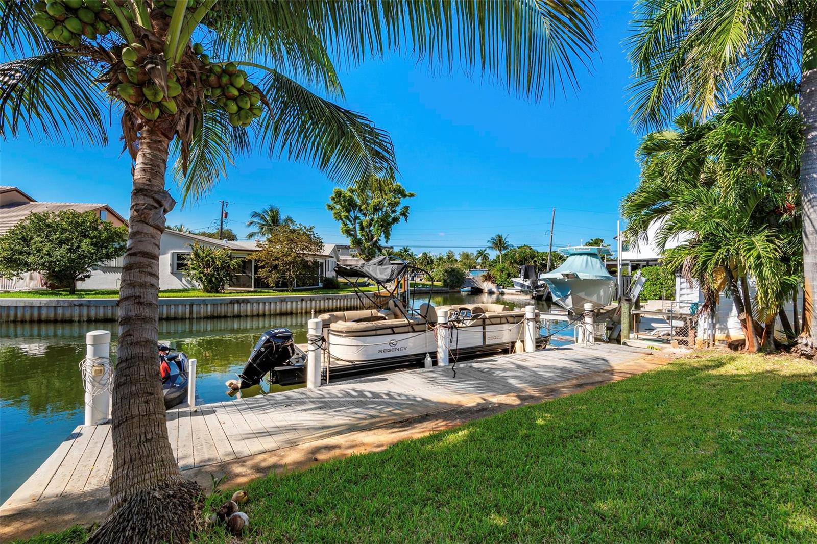 A pontoon boat is docked at a wooden pier along a canal lined with palm trees — 825 Argonaut Isle, Dania Beach FL 33004, DANIA BEACH, FL