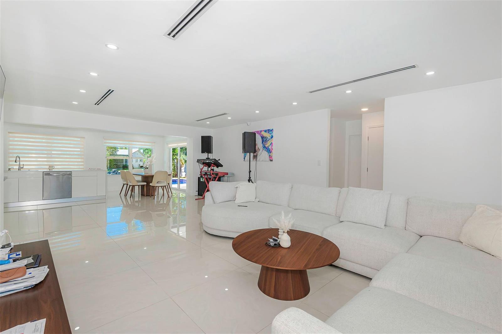 A white, open-concept living room features a large sectional sofa, tile floors, and a kitchen — 825 Argonaut Isle, Dania Beach FL 33004, DANIA BEACH, FL