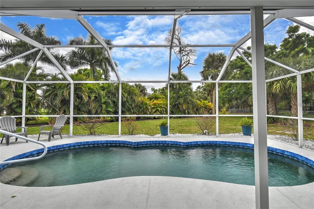 A screened-in pool patio features a kidney-shaped pool, two chairs, and lush tropical landscaping — 25101 KIMBERLY COURT, PUNTA GORDA, FL