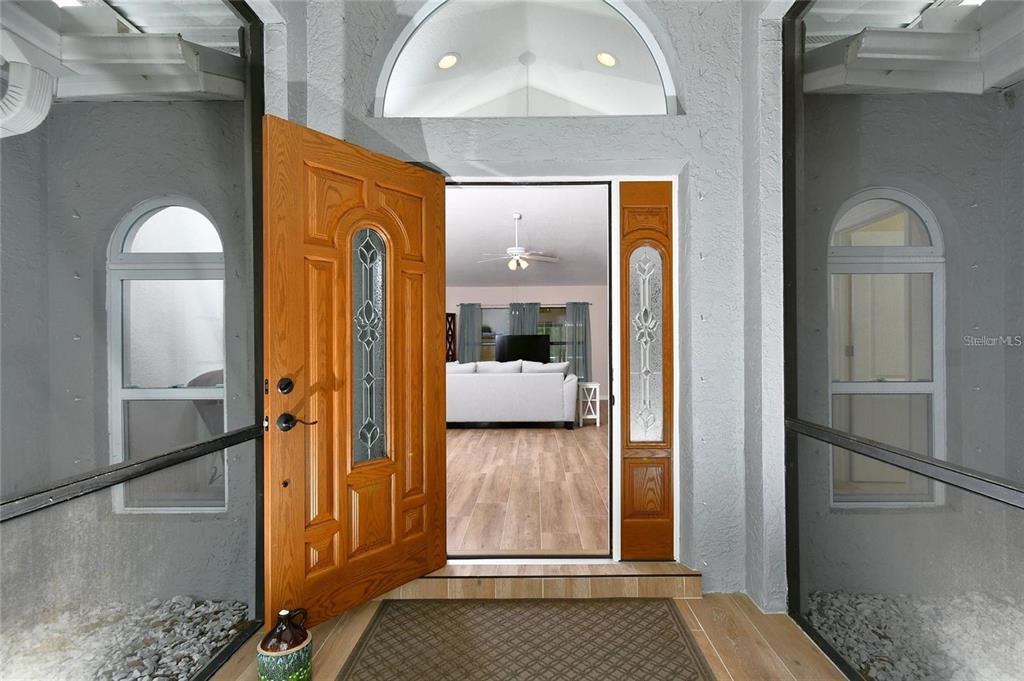 An open wooden front door reveals a living room with wood-look flooring and a ceiling fan — 25101 KIMBERLY COURT, PUNTA GORDA, FL