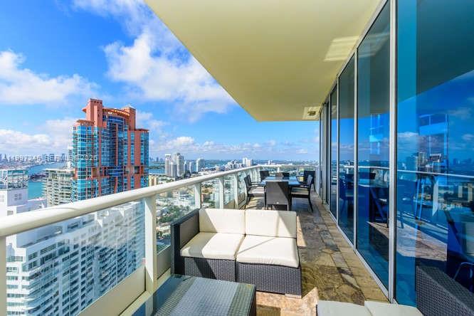 A high-rise balcony features wicker outdoor furniture, stone flooring, and panoramic city and water views — 100 S Pointe Dr # 3101, Miami Beach FL 33139, MIAMI BEACH, FL