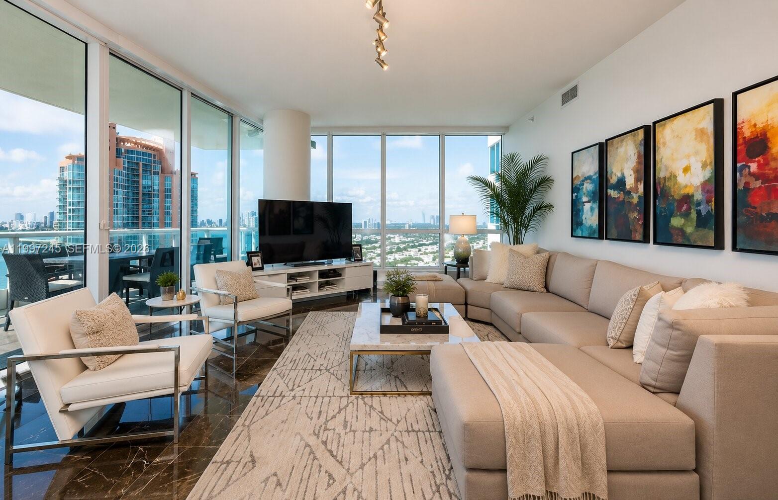 A modern living room features a large sectional sofa, floor-to-ceiling windows, and city views — 100 S Pointe Dr # 3101, Miami Beach FL 33139, MIAMI BEACH, FL