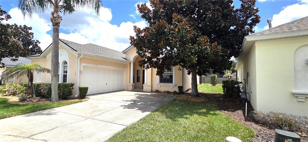 A single-story house with a beige stucco exterior, a two-car garage, and a large tree — 147 MINNIEHAHA CIRCLE, HAINES CITY, FL