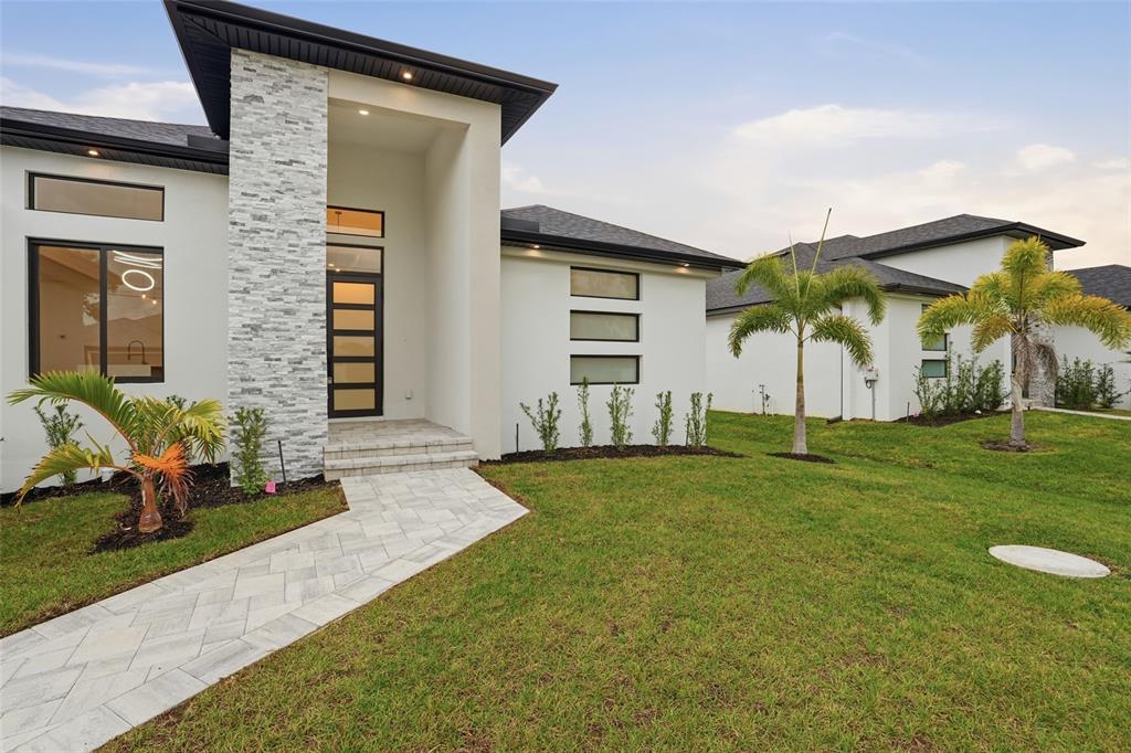 A modern single-story house with a stone-accented entryway, white stucco walls, and a paved walkway — 9402 ARRID CIRCLE, PORT CHARLOTTE, FL