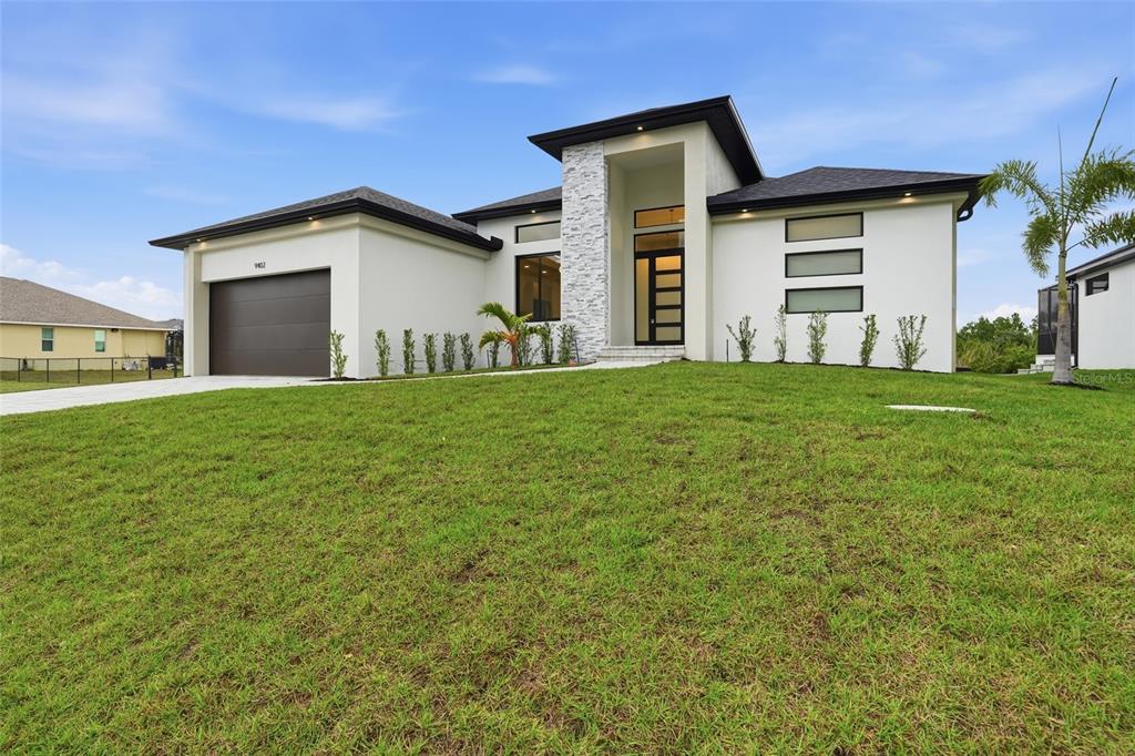 A modern single-story house with white stucco, a stone-accented entryway, and a dark garage door — 9402 ARRID CIRCLE, PORT CHARLOTTE, FL