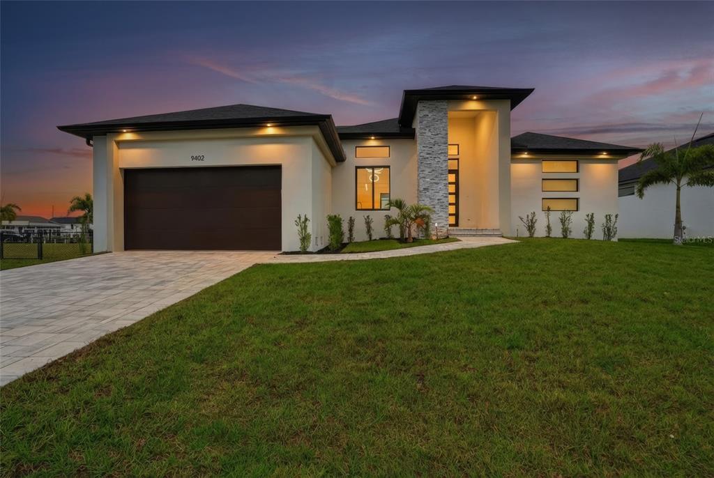 A modern single-story house with a stone-accented entryway and a two-car garage at dusk — 9402 ARRID CIRCLE, PORT CHARLOTTE, FL