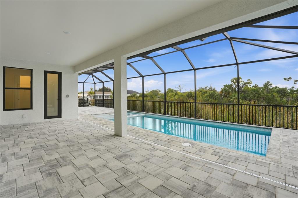 A covered patio with stone pavers overlooks a screened-in swimming pool and natural landscape — 9402 ARRID CIRCLE, PORT CHARLOTTE, FL