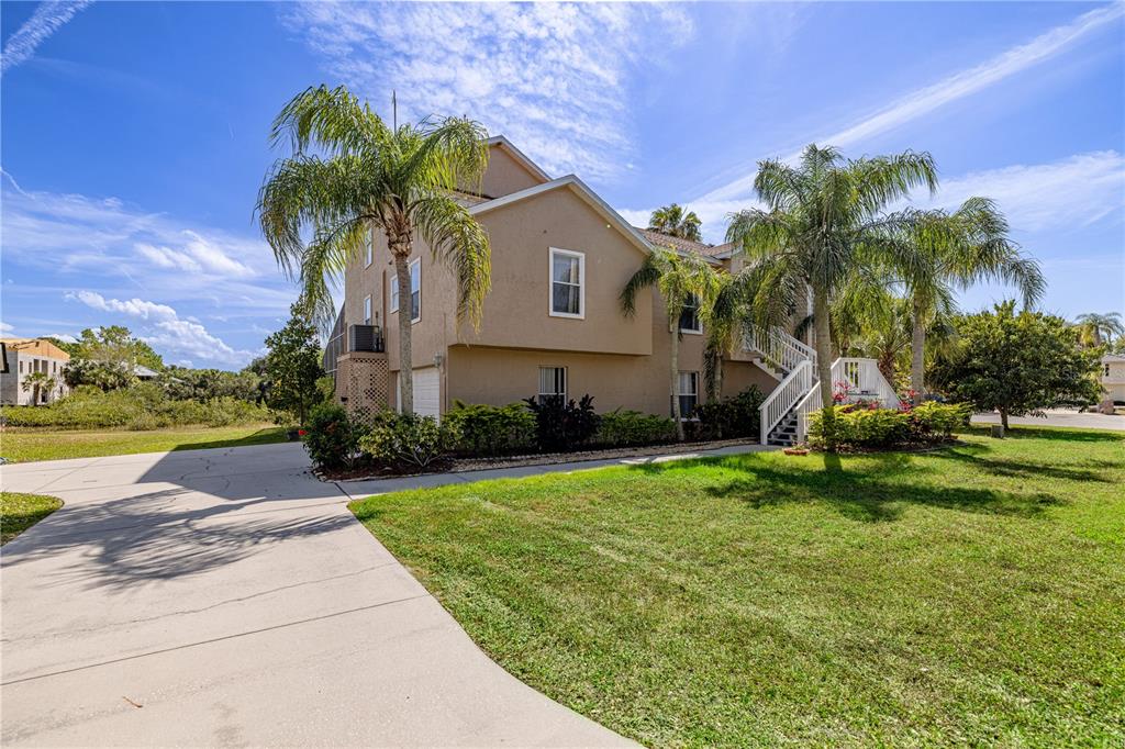 A two-story tan house with a concrete driveway, palm trees, and an outdoor staircase — 7345 BRIGHTWATERS COURT, NEW PORT RICHEY, FL