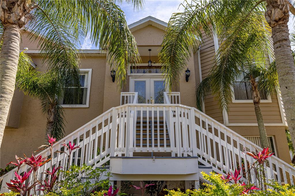A tan house exterior features a white wooden staircase leading to a double front door — 7345 BRIGHTWATERS COURT, NEW PORT RICHEY, FL