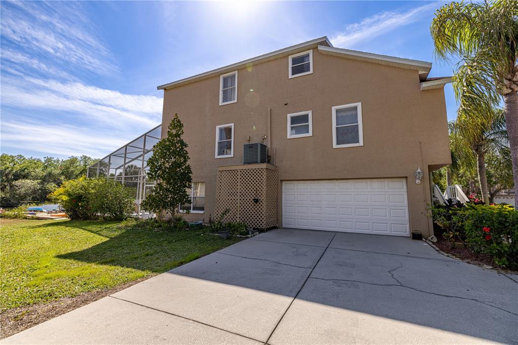 The exterior of a two-story house features a concrete driveway, a garage, and a pool enclosure — 7345 BRIGHTWATERS COURT, NEW PORT RICHEY, FL