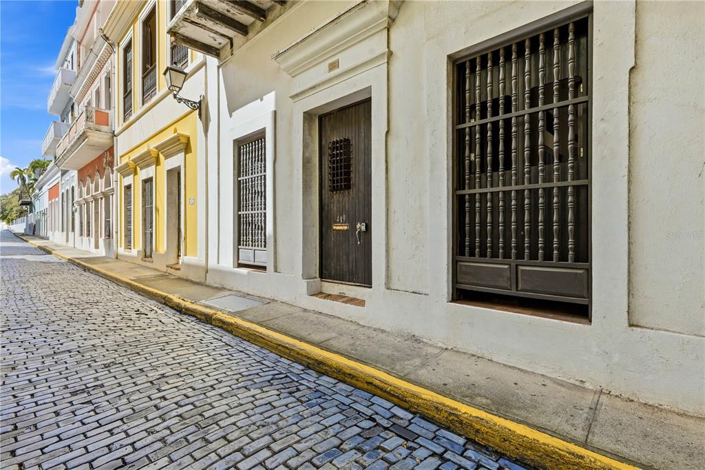 A cobblestone street runs alongside a row of historic buildings with wooden doors and shutters — 418-419 NORZAGARAY AND SOL STREETS, SAN JUAN, PR