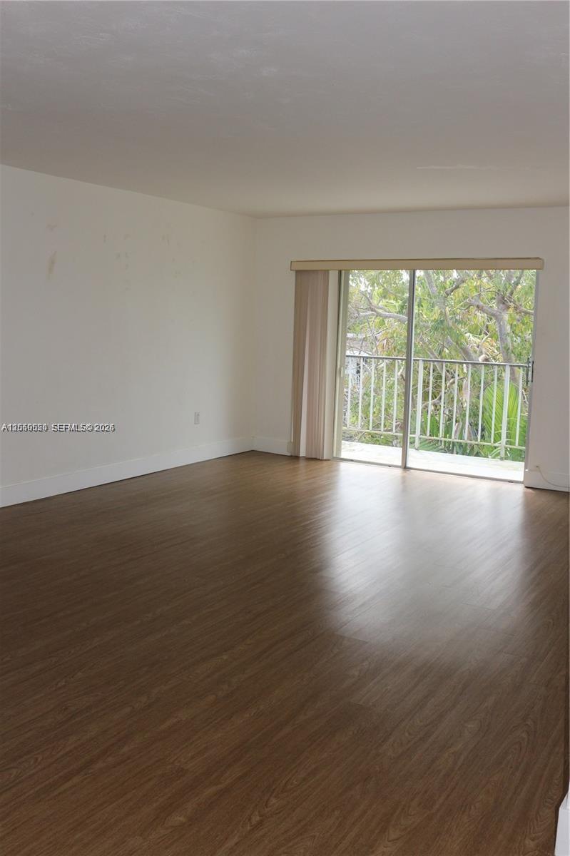 An empty room features wood-look flooring, white walls, and a sliding glass door to a balcony — 9611 SW 77th Ave # 306A, Miami FL 33156, MIAMI, FL