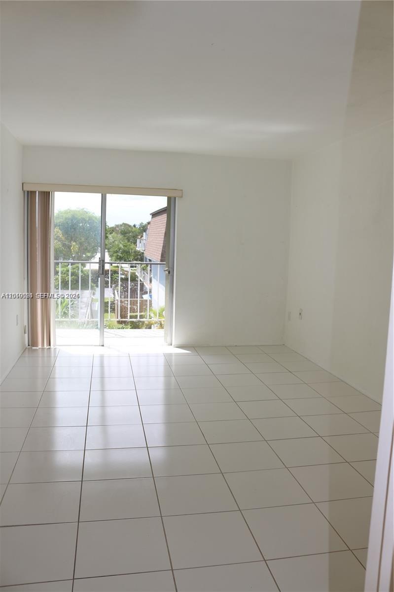 An empty room with white tile floors and a sliding glass door leading to a balcony — 9611 SW 77th Ave # 306A, Miami FL 33156, MIAMI, FL