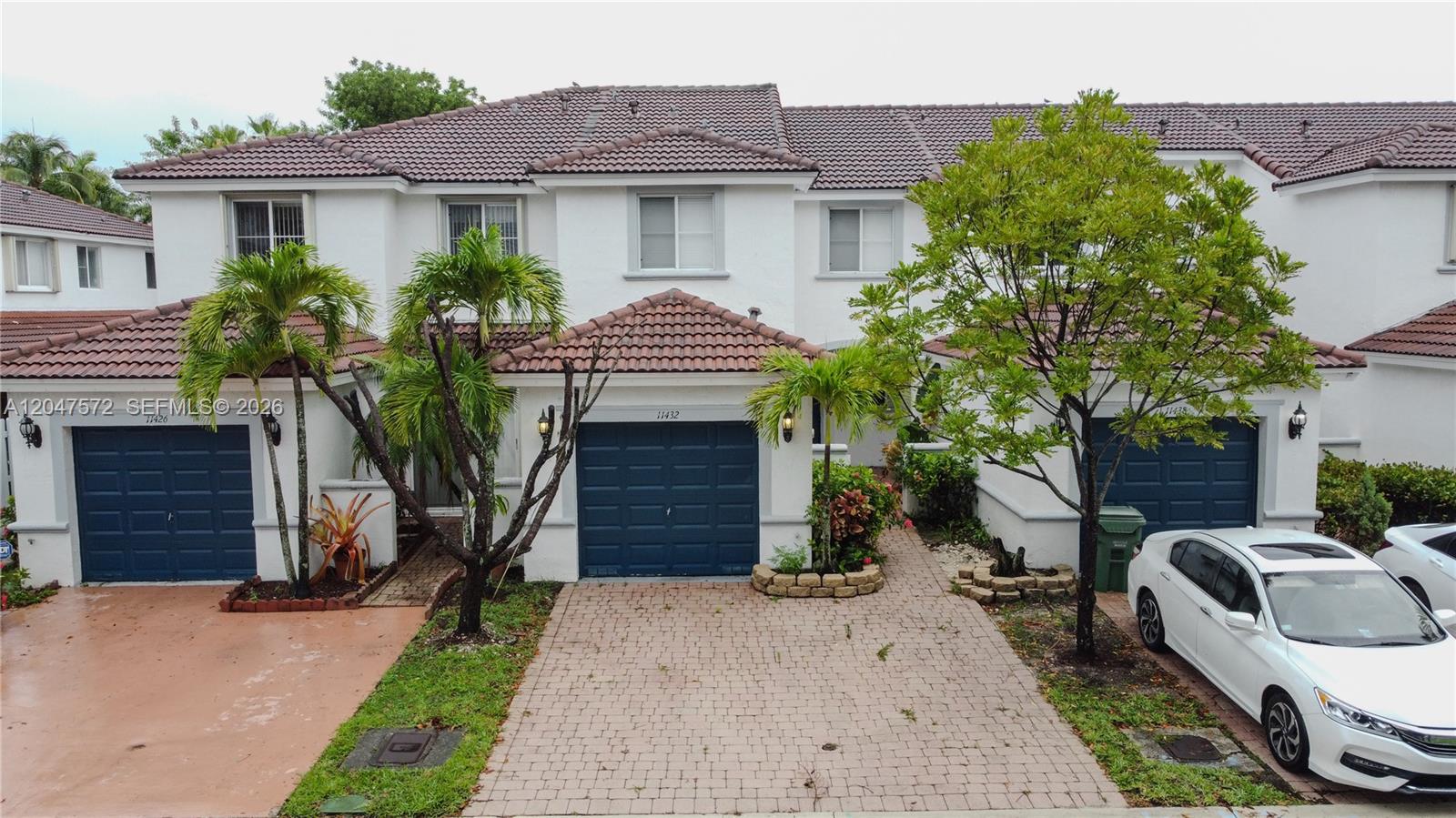 An exterior view of a two-story townhouse complex with blue garage doors and tile roofs — 11432 NW 48th Ter, Doral FL 33178, DORAL, FL