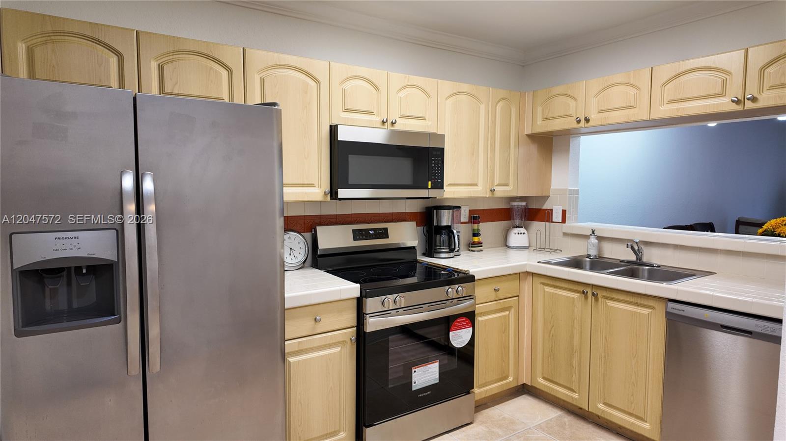 A kitchen features light wood cabinets, stainless steel appliances, and white tiled countertops — 11432 NW 48th Ter, Doral FL 33178, DORAL, FL