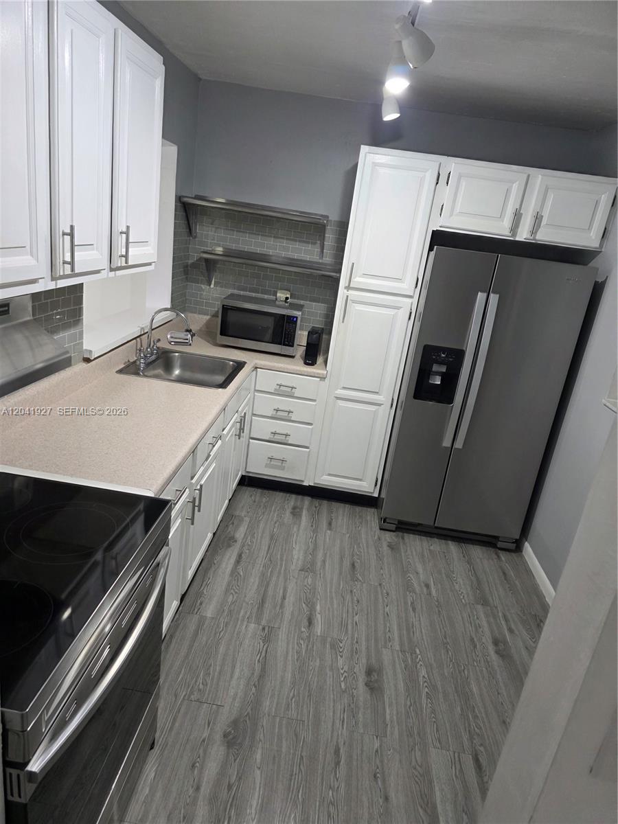A kitchen features white cabinets, stainless steel appliances, a gray tiled backsplash, and wood-look flooring — 8065 SW 107th Ave # 202, Miami FL 33173, MIAMI, FL