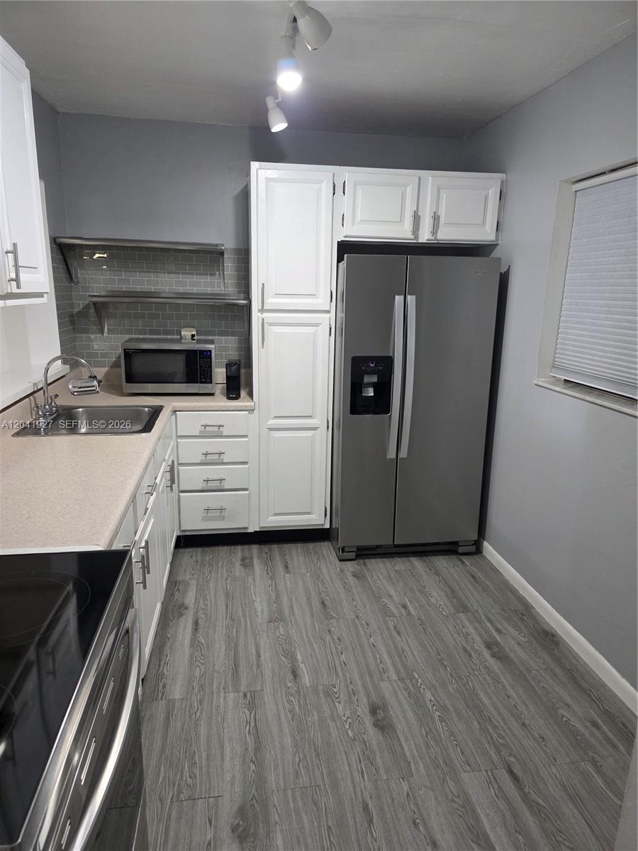 A kitchen features stainless steel appliances, white cabinetry, gray walls, and wood-look flooring — 8065 SW 107th Ave # 202, Miami FL 33173, MIAMI, FL