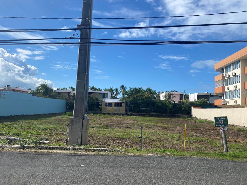 A vacant, fenced-in rectangular lot sits between a blue wall and a multi-story building — 16 OCEAN DRIVE AVENUE LOT A, LUQUILLO, PR