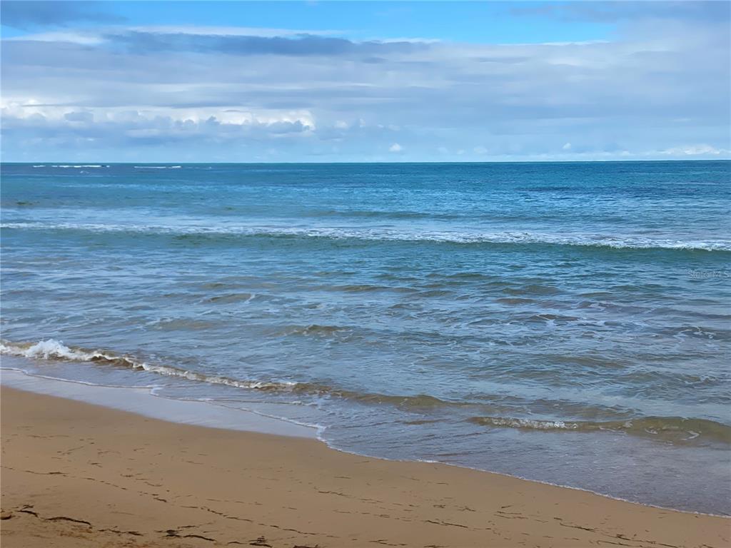 A sandy beach meets the ocean under a cloudy blue sky — 16 OCEAN DRIVE AVENUE LOT A, LUQUILLO, PR