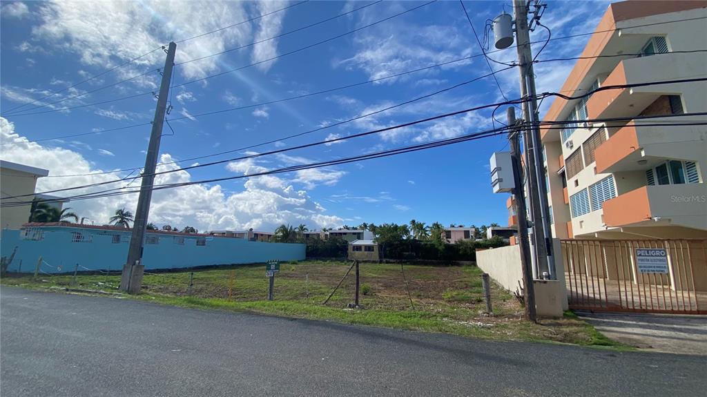 A vacant, fenced-in lot sits between a light blue wall and a multi-story apartment building — 16 OCEAN DRIVE AVENUE LOT A, LUQUILLO, PR