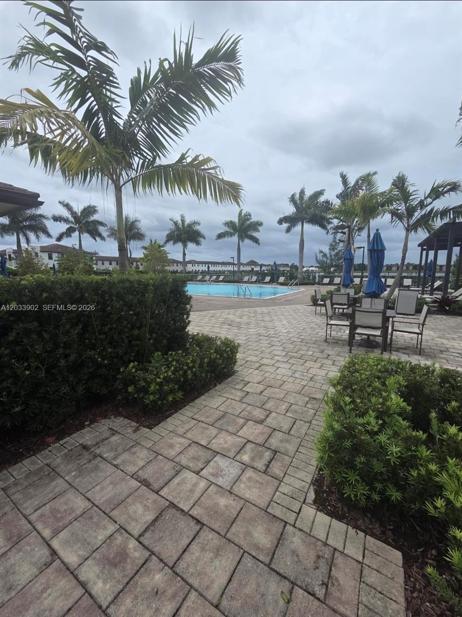 A paved patio area features outdoor seating and palm trees overlooking a swimming pool — 21124 NE 8th Ave, Miami FL 33179, MIAMI, FL