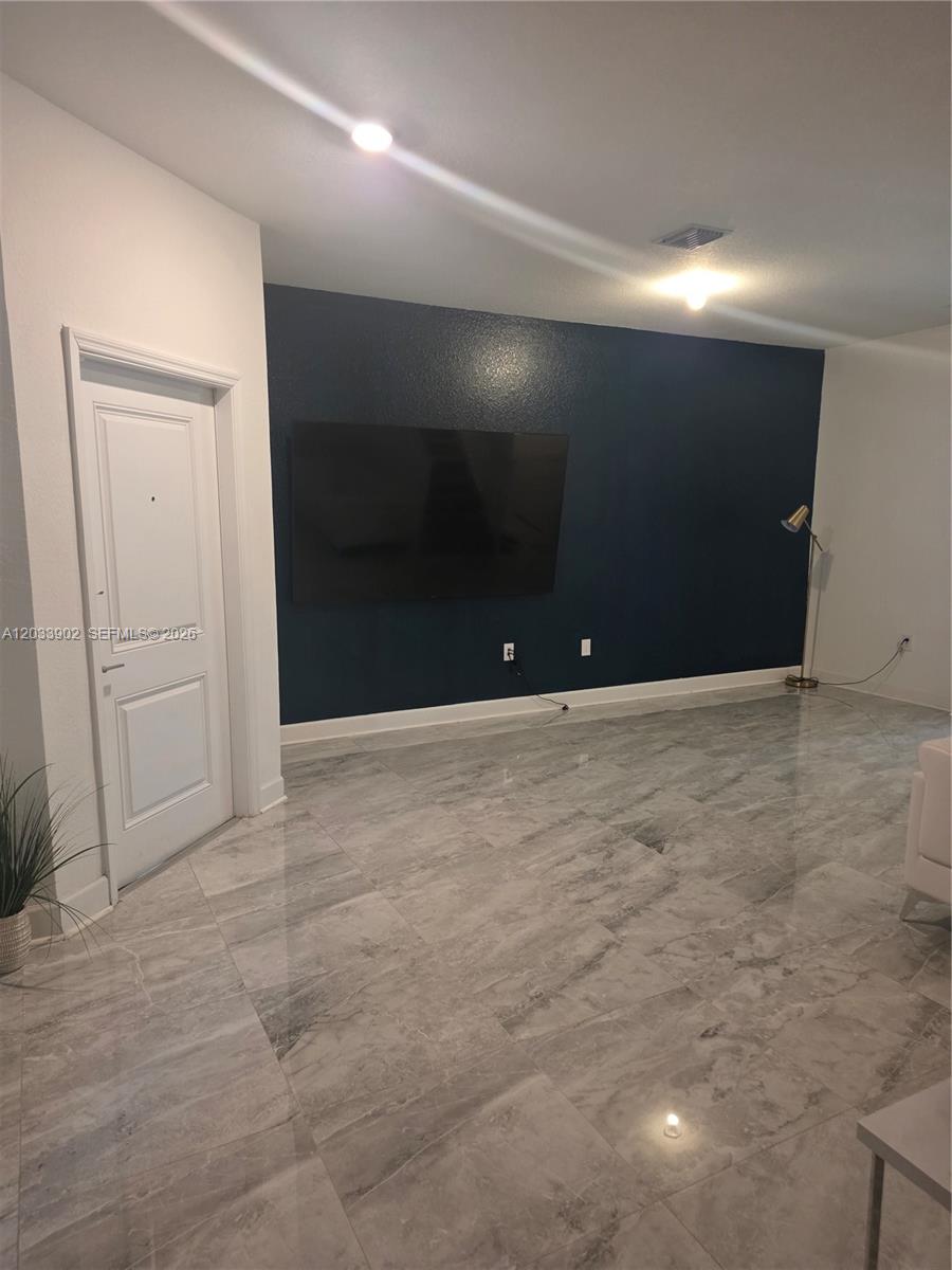A living room features a dark blue accent wall, a wall-mounted television, and gray tile flooring — 21124 NE 8th Ave, Miami FL 33179, MIAMI, FL