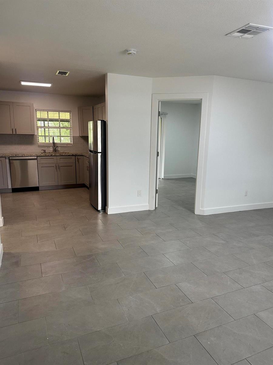A kitchen with gray cabinets and stainless steel appliances opens into a tiled living area — 4786 Cambridge Street, FL 33463, FL