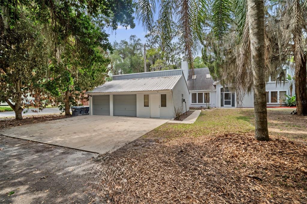 A detached two-car garage with a metal roof sits beside a white residential house — 130 N CARPENTER ROAD, TITUSVILLE, FL