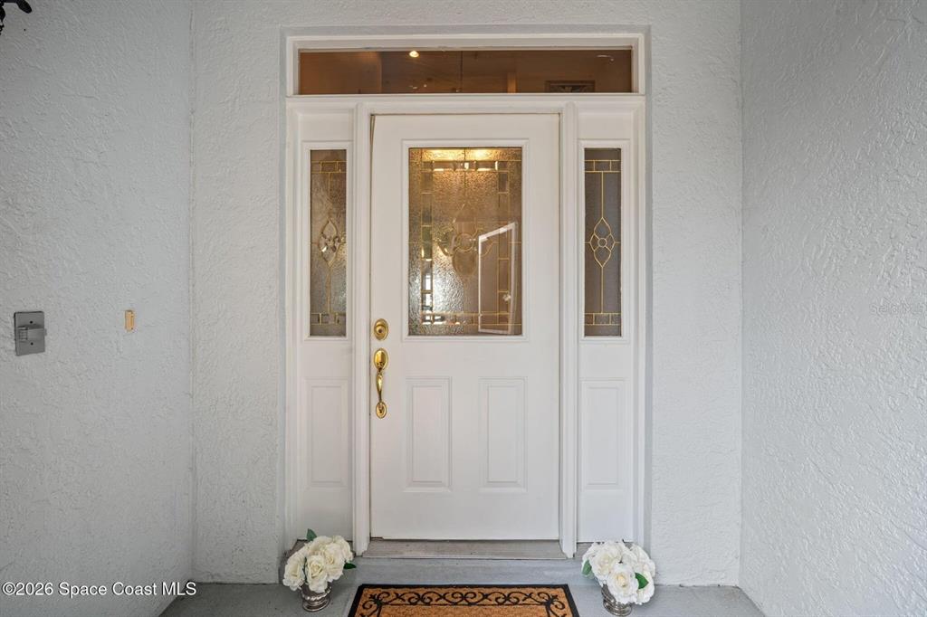 A white front door with a glass insert and sidelights is set in a stucco wall — 130 N CARPENTER ROAD, TITUSVILLE, FL
