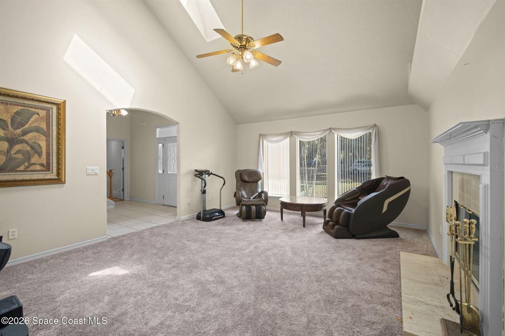 A living room features a vaulted ceiling, carpeted flooring, a fireplace, and a ceiling fan — 130 N CARPENTER ROAD, TITUSVILLE, FL