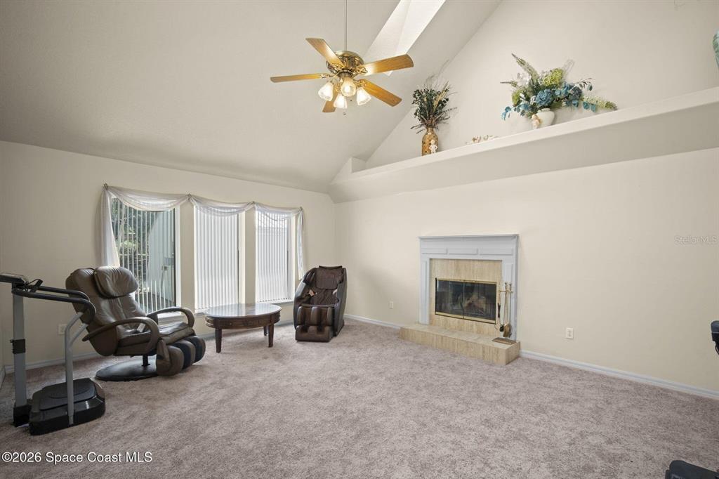 A living room features a vaulted ceiling, a fireplace, and carpeted flooring — 130 N CARPENTER ROAD, TITUSVILLE, FL