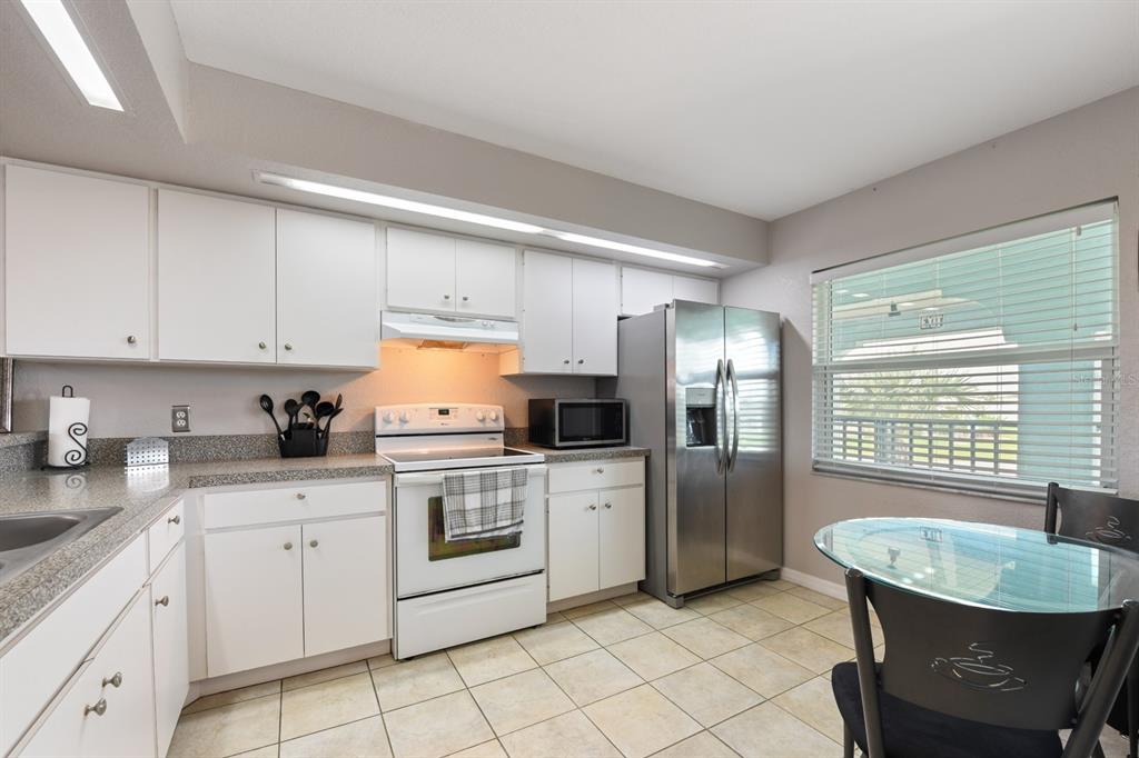 A kitchen features white cabinets, stainless steel appliances, granite countertops, and a small dining area — 449 ROYAL POINCIANA UNIT 221, PUNTA GORDA, FL