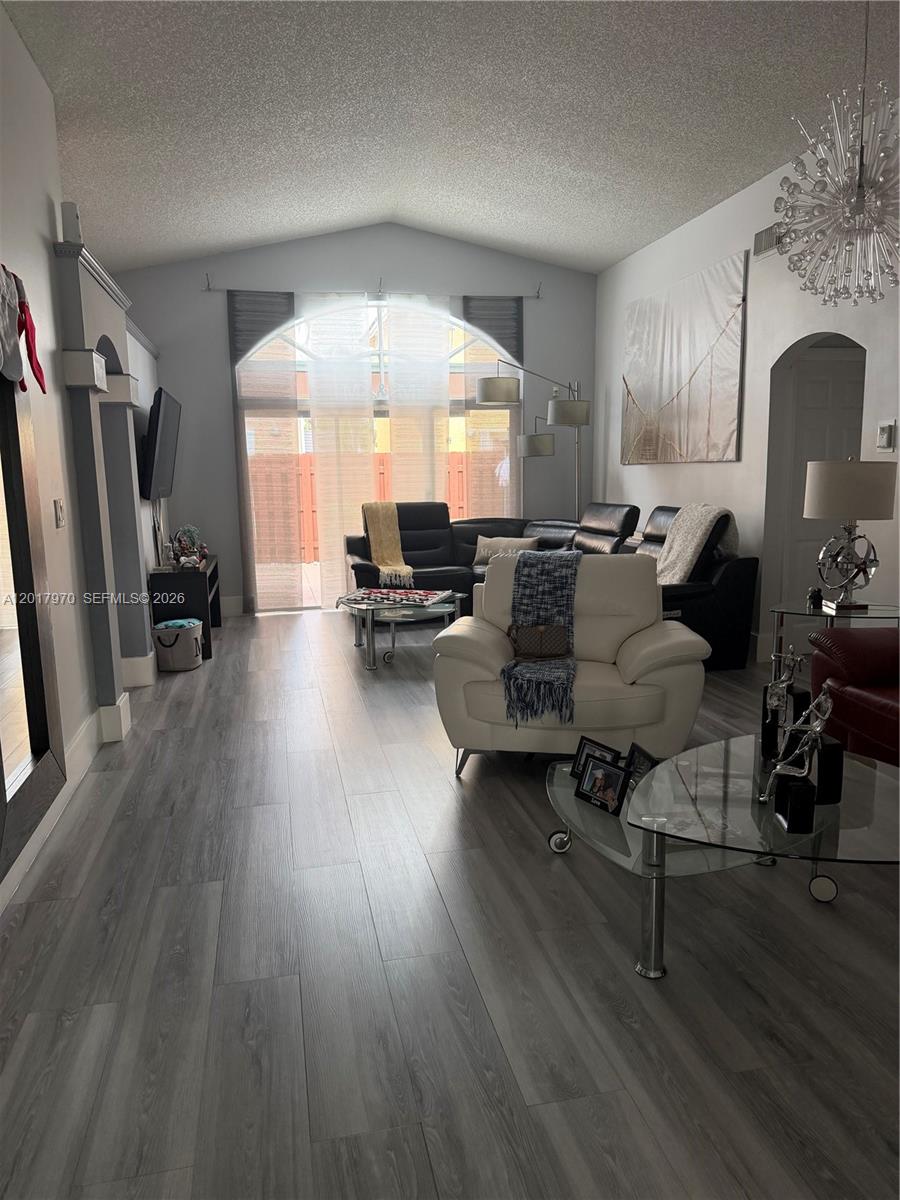 A living room features vaulted ceilings, gray wood-look flooring, and a large arched window — 15823 SW 82nd St, Miami FL 33193, MIAMI, FL
