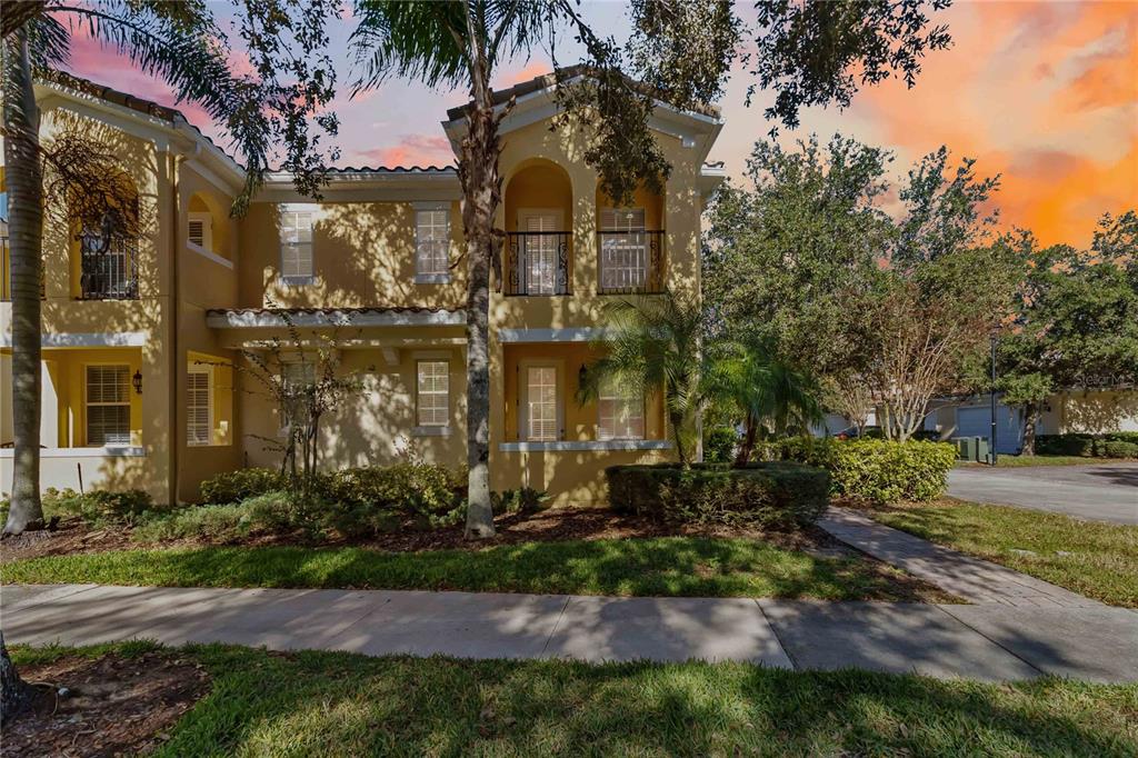 A two-story yellow stucco townhouse features arched balconies, a palm tree, and a sidewalk — 8681 LOWER VILLAGEWALK CIRCLE, ORLANDO, FL