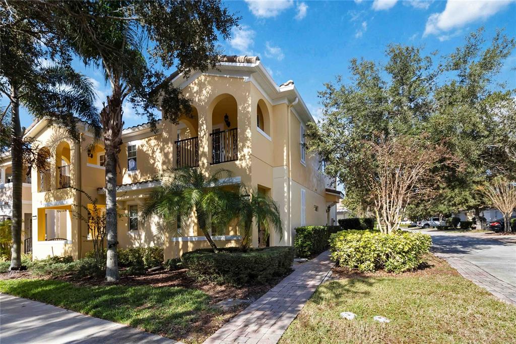 A two-story yellow stucco townhouse with a balcony and a sidewalk in the foreground — 8681 LOWER VILLAGEWALK CIRCLE, ORLANDO, FL