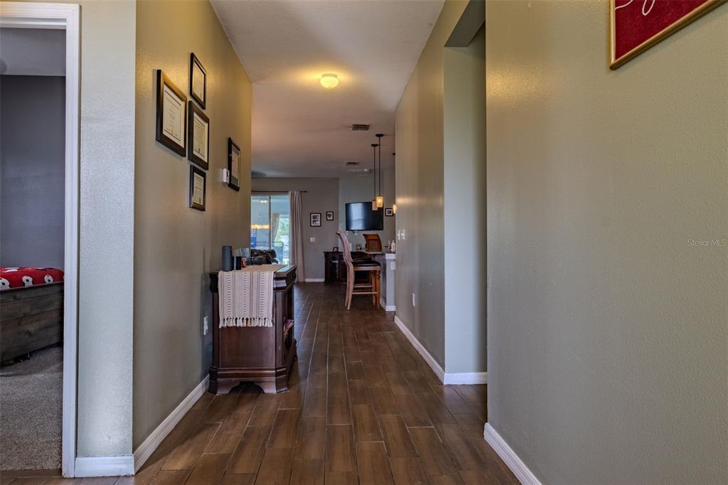 A hallway with wood-look tile flooring leads toward an open kitchen and living area — 4379 MOON SHADOW LOOP, MULBERRY, FL