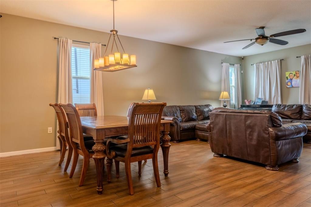 A dining area with a wooden table and chairs sits adjacent to a living room — 4379 MOON SHADOW LOOP, MULBERRY, FL