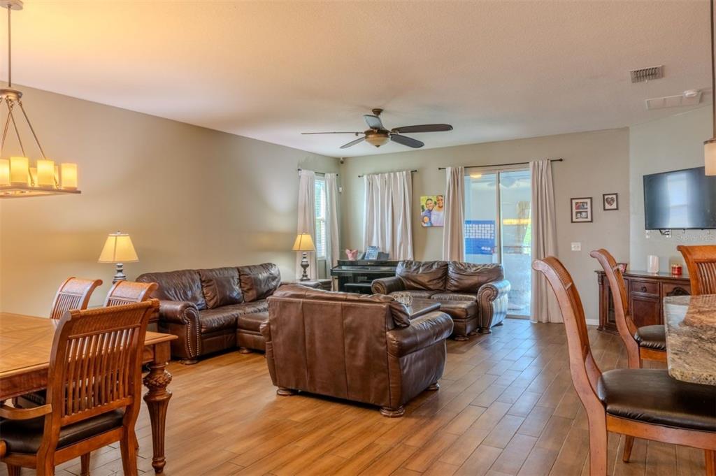 An open-concept living and dining area features brown leather furniture, wood-look tile flooring, and a ceiling fan — 4379 MOON SHADOW LOOP, MULBERRY, FL