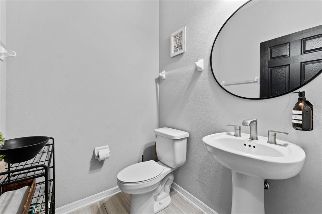 A small bathroom features a pedestal sink, a toilet, and a round wall mirror — 29913 SOUTHWELL LANE, WESLEY CHAPEL, FL