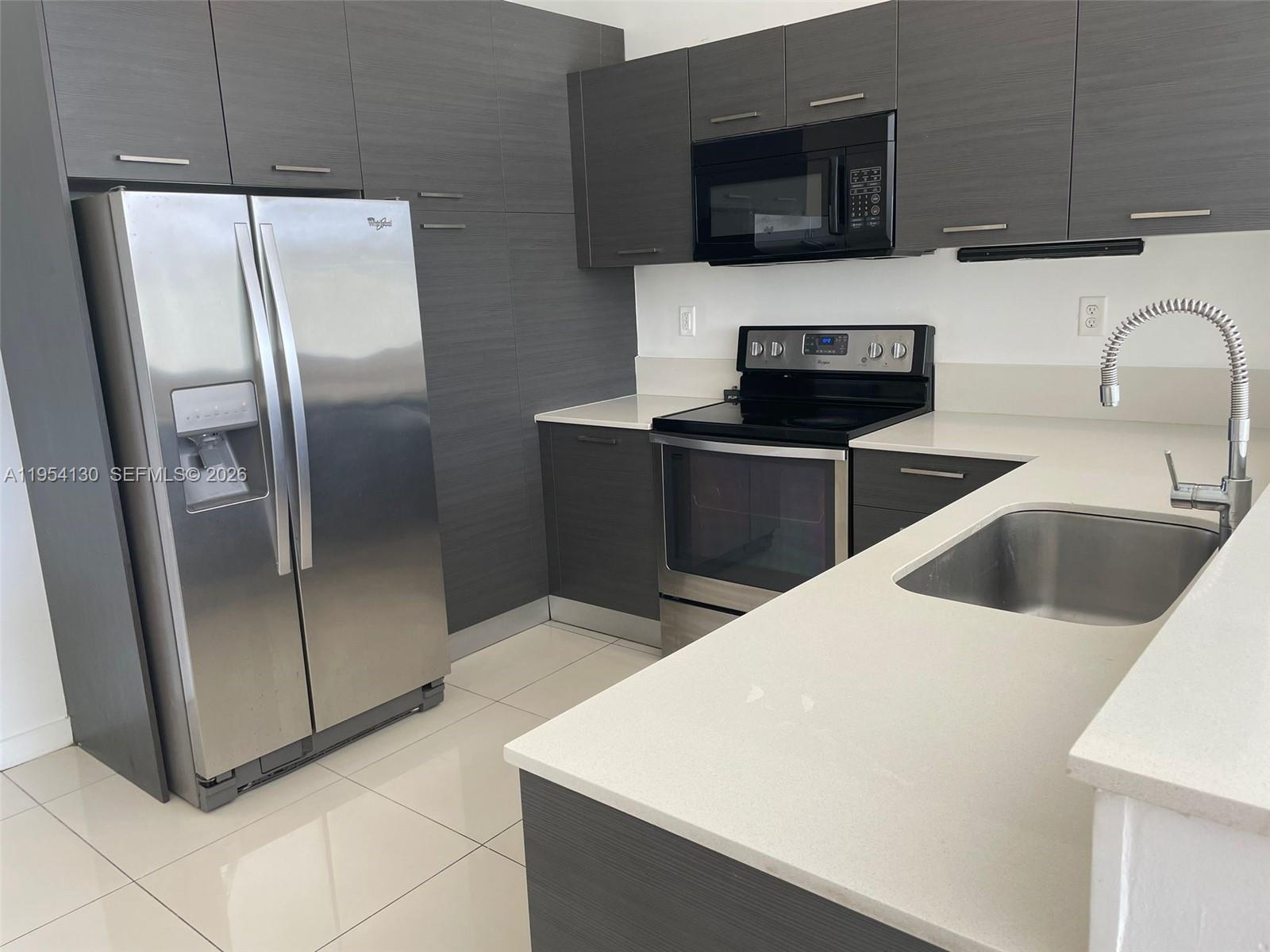 A modern kitchen features dark wood-grain cabinets, stainless steel appliances, and white quartz countertops — 3486 NW 13th St # 3486, Lauderhill FL 33311, LAUDERHILL, FL