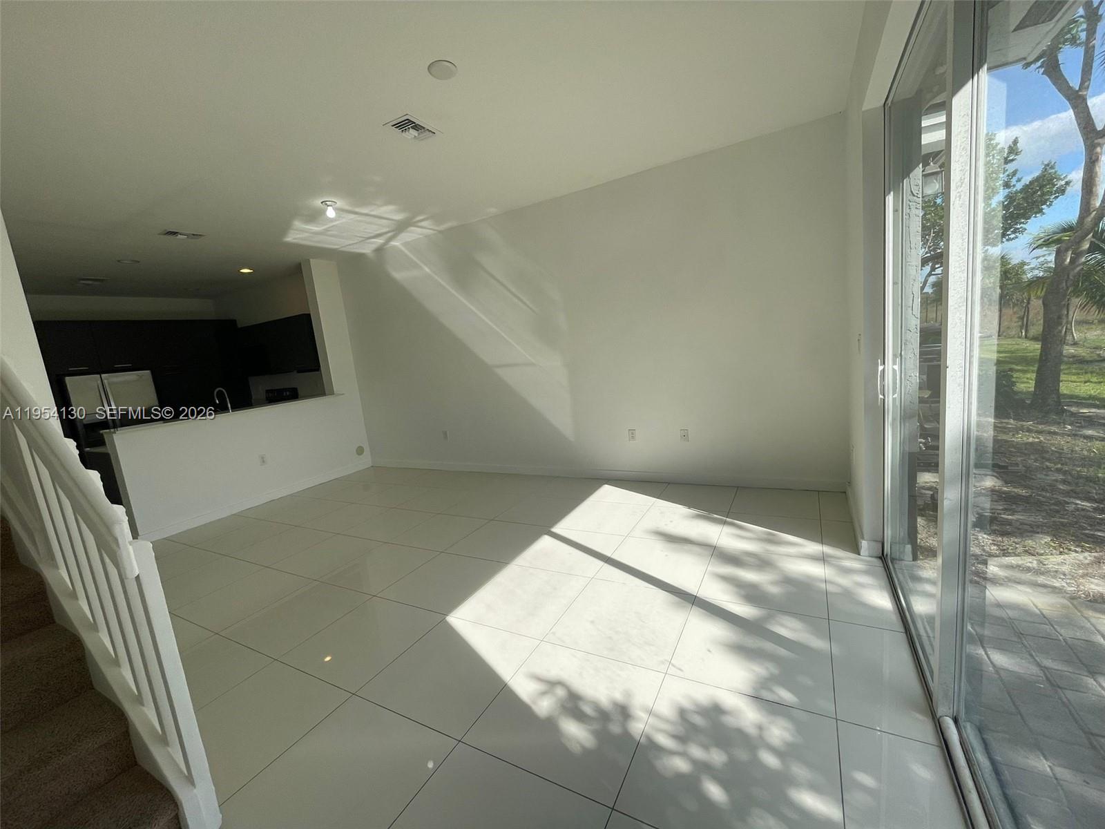 A bright living room features white tile floors, a kitchen pass-through, and sliding glass doors — 3486 NW 13th St # 3486, Lauderhill FL 33311, LAUDERHILL, FL