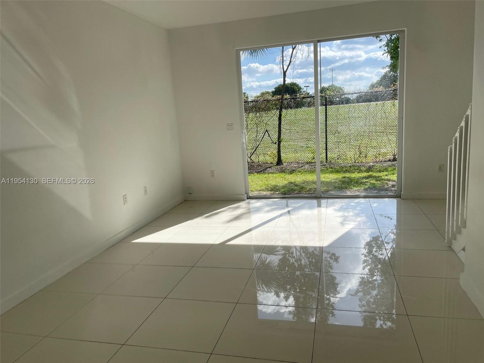 An empty room with white tile floors and a sliding glass door leading outside — 3486 NW 13th St # 3486, Lauderhill FL 33311, LAUDERHILL, FL