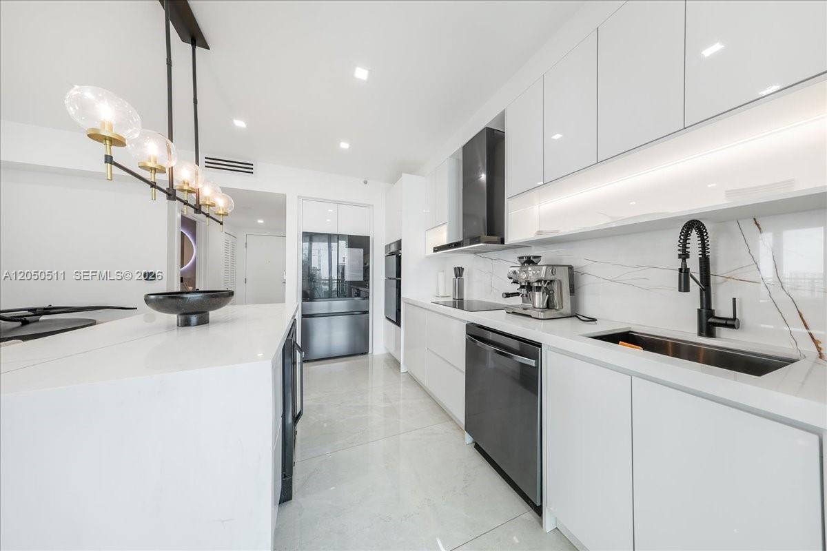 A modern kitchen features white cabinetry, marble-style backsplash, stainless steel appliances, and a central island — 350 S Miami Ave # 2314, Miami FL 33130, MIAMI, FL