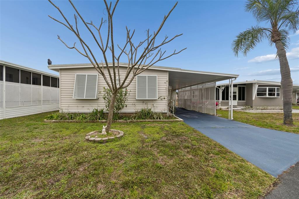 A single-story manufactured home with a carport, light siding, and a bare tree in front — 678 MOUNT MADISON AVENUE NE UNIT 661, ST PETERSBURG, FL