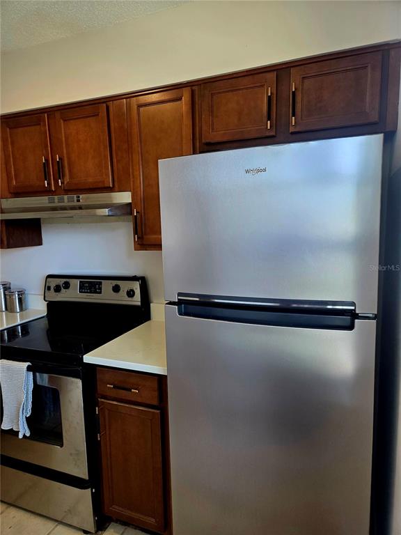 A kitchen features dark wood cabinets, a stainless steel refrigerator, and a matching electric range — 13719 MISSION OAKS BOULEVARD UNIT 0, SEMINOLE, FL