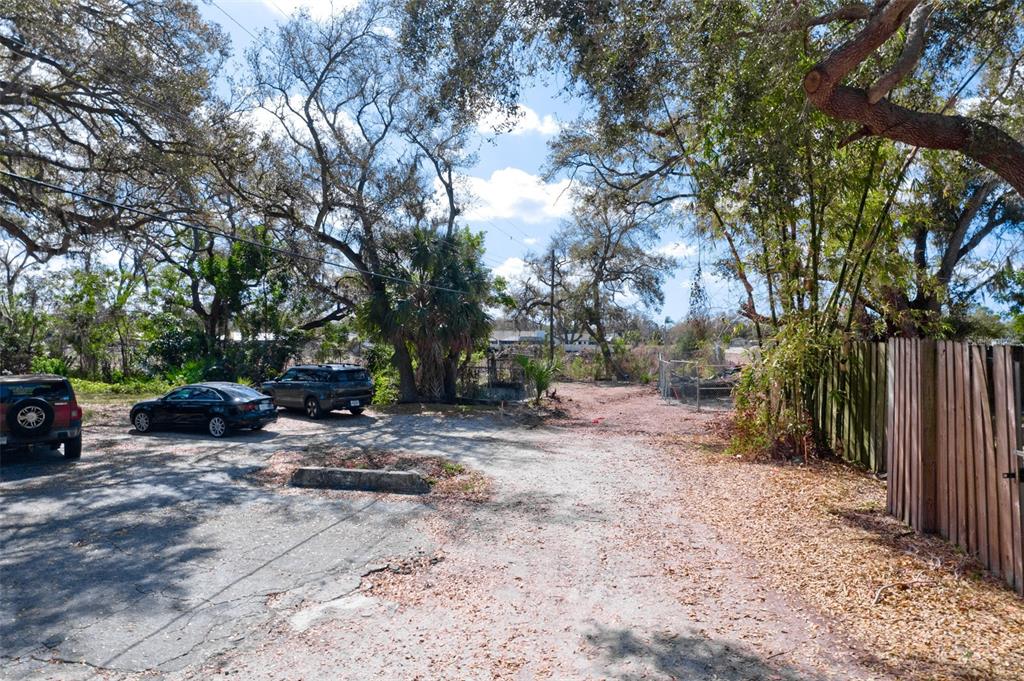 A gravel parking area sits beneath large trees next to a wooden fence — 4101 S SCHOOL AVENUE, SARASOTA, FL