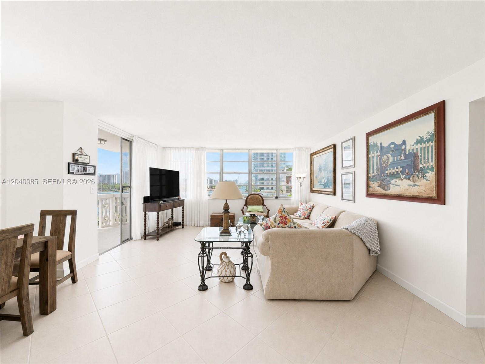 A living room with tile floors, a beige sofa, and a balcony overlooking the water — 1817 S Ocean Dr # 620, Hallandale Beach FL 33009, HALLANDALE BEACH, FL